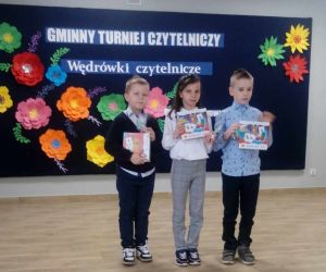 Troje uczniów klasy drugiej i pierwszej na tle tablicy dekoracyjnej