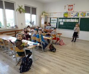 Uczennica w roli nauczyciela siedzi przed uczniami klasy II