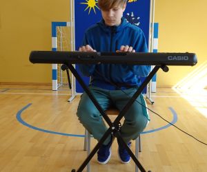 Uczeń siedzi na krześle i gra na instrumencie klawiszowym