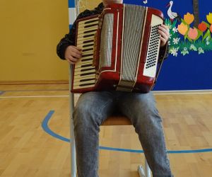 Uczeń siedzi na krześle i gra na akordeonie