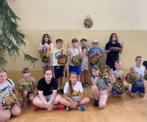 Zdjęcie przedstawia grupę dzieci wewnątrz budynku, trzymające w rękach samodzielnie wykonany dekoracyjny plaster drewna.