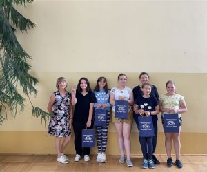 Zdjęcie przedstawia grupę dzieci wewnątrz budynku oraz dwie osoby dorosłe. Wszyscy stoją pod ścianą, dzieci trzymają torby papierowe z napisem GOK, w których dostały nagrody w konkursie.