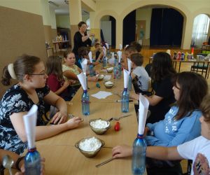 Zdjęcie przedstawia grupę dzieci wewnątrz budynku oraz osobę dorosłą. Dzieci wykonują 