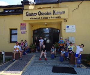 Zdjęcie przedstawia grupę dzieci przed budynkiem z napisem: Gminny Ośrodek Kultury w Hrubieszowie z siedzibą w Wołajowicach. 