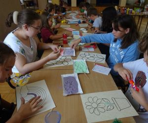 Zdjęcie przedstawia grupę dzieci wewnątrz budynku. Dzieci wykonują prace plastyczną - malowanie solą.