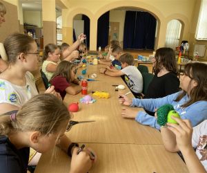Zdjęcie przedstawia grupę dzieci wewnątrz budynku. Dzieci wykonują prace plastyczną - gniotki.