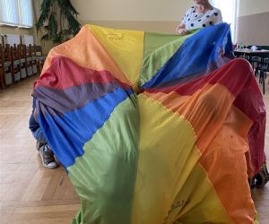 Zdjęcie przedstawia dzieci wewnątrz budynku bawiące się chusta animacyjną.