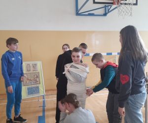 Uczniowie owijają bandażami jednego z chłopców, tworząc mumię