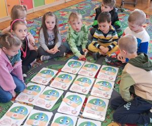 Dzieci siedzą na dywanie, oglądają ilustracje na temat ziemi.