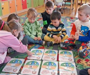 Dzieci siedzą na dywanie, oglądają ilustracje na temat ziemi.