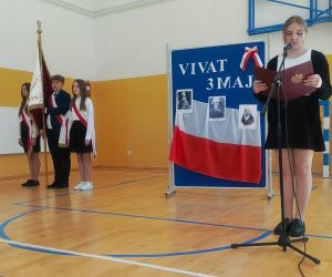 Uczennica klasy siódmej śpiewa przy mikrofonie, w tle poczet sztandarowy