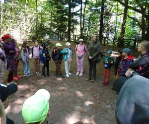 Uczniowie stoją w kręgu z przewodniczką pośród drzew