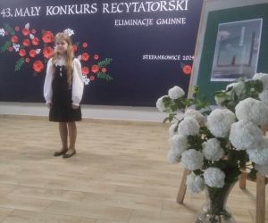 Uczennica recytuje na scenie na tle tablicy dekoracyjnej