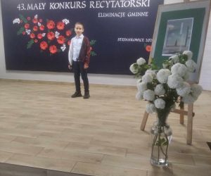 Uczeń recytuje na scenie na tle tablicy dekoracyjnej