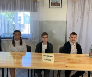 Troje uczniów siedzi przy stole przed konkursem