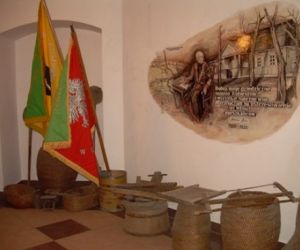 Kolorowe sztandary, drewniane narzędzia i beczki, mural przedstawiający człowieka na tle starej chaty