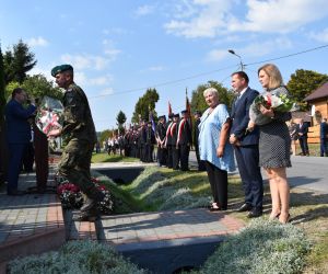 Osoby składają kwiaty przy pomniku. 