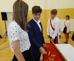 Uczeń i uczennica wbijają pamiątkowy gwóźdź do drzewca sztandaru