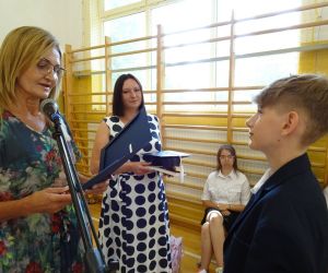 Dyrektor szkoły i wychowawczyni klasy ósmej wręczają uczniowi świadectwo i biret