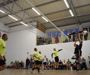 Zdjęcie przedstawia drużyny rozgrywające mecz piłki siatkowej, który odbywa się na hali sportowej.