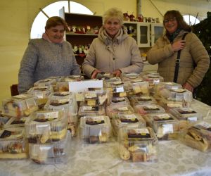 Na zdjęciu znajdują się osoby stojące przy stoisku z ciastem.