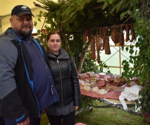 Na zdjęciu znajdują się dwie osoby na świeżym powietrzu, przy stoisku ze swojskim jadłem.
