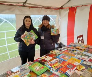 Na zdjęciu znajdują się dwie kobiety, na powietrzu pod namiotem, stojące przy stoisku z używanymi książkami.
