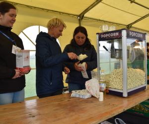Na zdjęciu znajdują się trzy osoby i maszyna do popcornu.