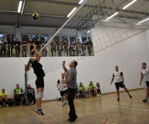 Zdjęcie przedstawia drużyny rozgrywające mecz piłki siatkowej, który odbywa się na hali sportowej.