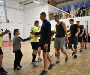 Zdjęcie przedstawia drużyny rozgrywające mecz piłki siatkowej, który odbywa się na hali sportowej.