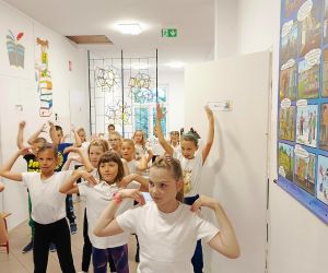 Uczniowie klas młodszych podczas rozgrzewki sportowej na korytarzu szkolnym