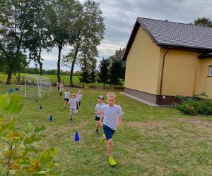 Uczniowie klas młodszych biegną w szeregu wokół boiska szkolnego