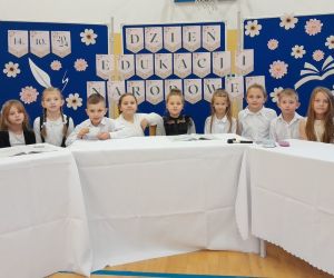 Uczniowie klasy pierwszej  przy stole na tle dekoracji okolicznościowej