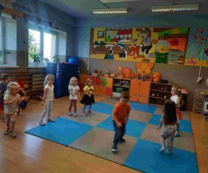 Przedszkolaki w ubraniach w kropki bawią się pod kierunkiem nauczycielki