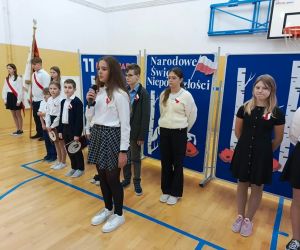 Uczennica recytuje do mikrofonu stojąc przed szeregiem pozostałych uczniów