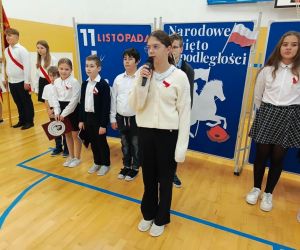 Uczennica recytuje do mikrofonu stojąc przed szeregiem pozostałych uczniów