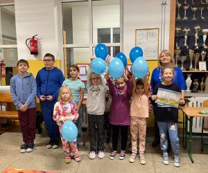 Nauczycielka i uczniowie ubrani na niebiesko trzymają w ręku niebieskie balony