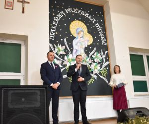 Trzy osoby stoją na scenie wewnątrz budynku.