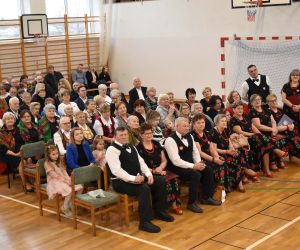 Publicznośc wewnątrz budynku. Ludzie siedza na sali na krzesłach.