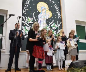 Grupa osób na scenie wewnątrz budynku. Odbiór statuetek, laureaci Konkursu.